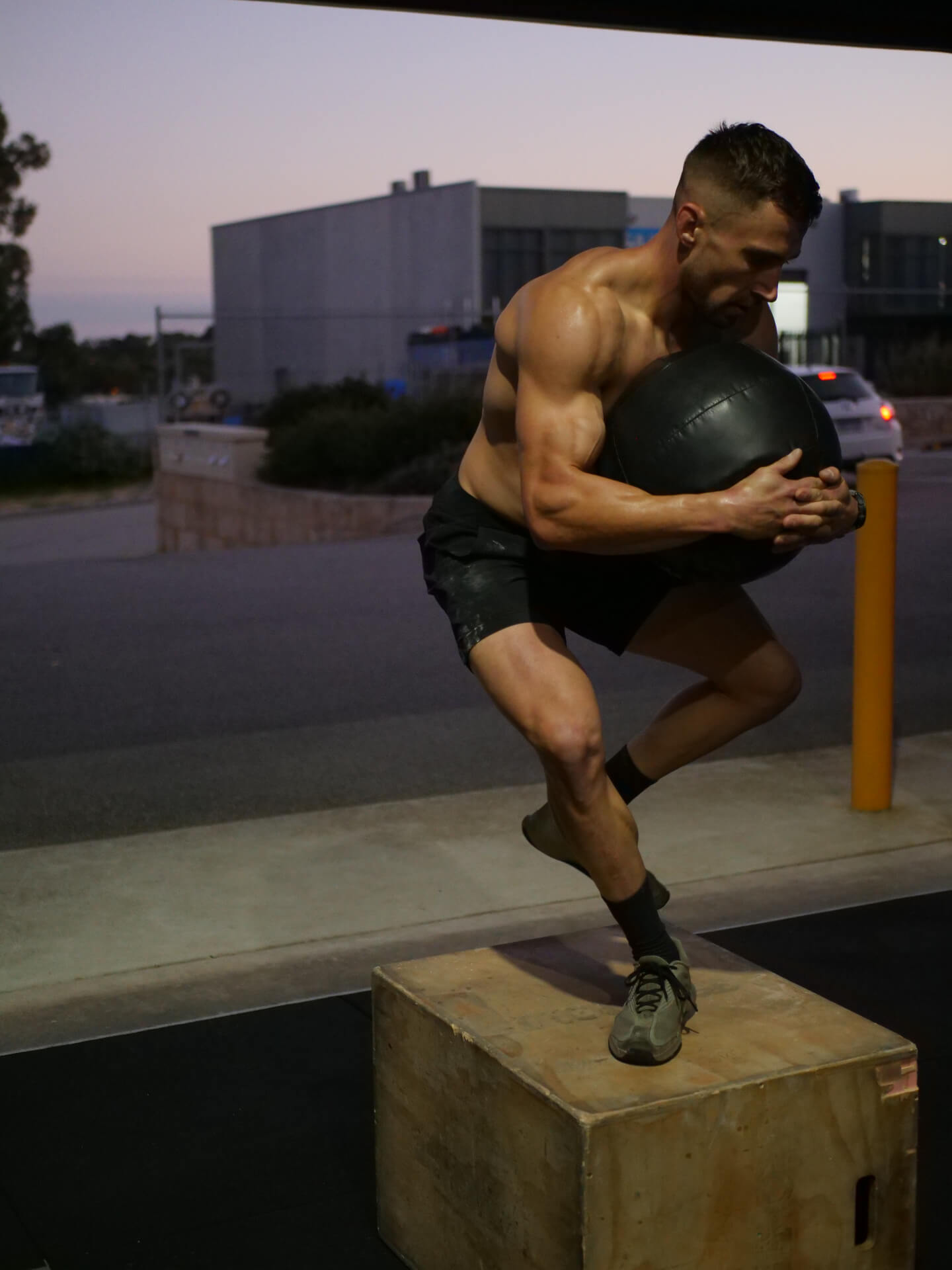 Member stepping onto a box holding a wall ball at dusk outside the gym